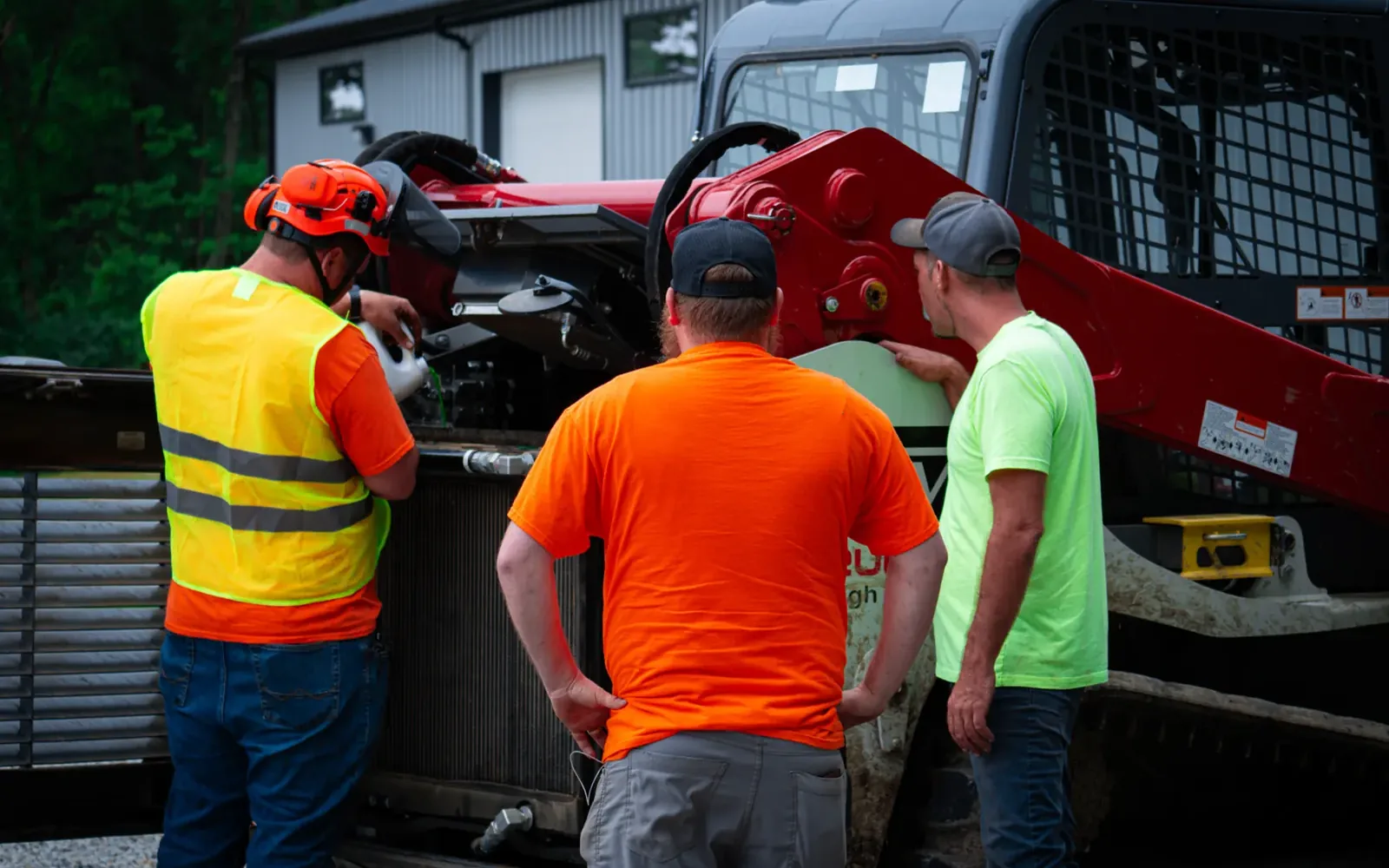 Brushworks crew gathered around a track loader at the shop