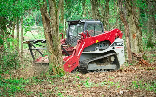 Takeuchi track loader with a Fecon mulching head working along a wooded edge, the cleared floor behind it