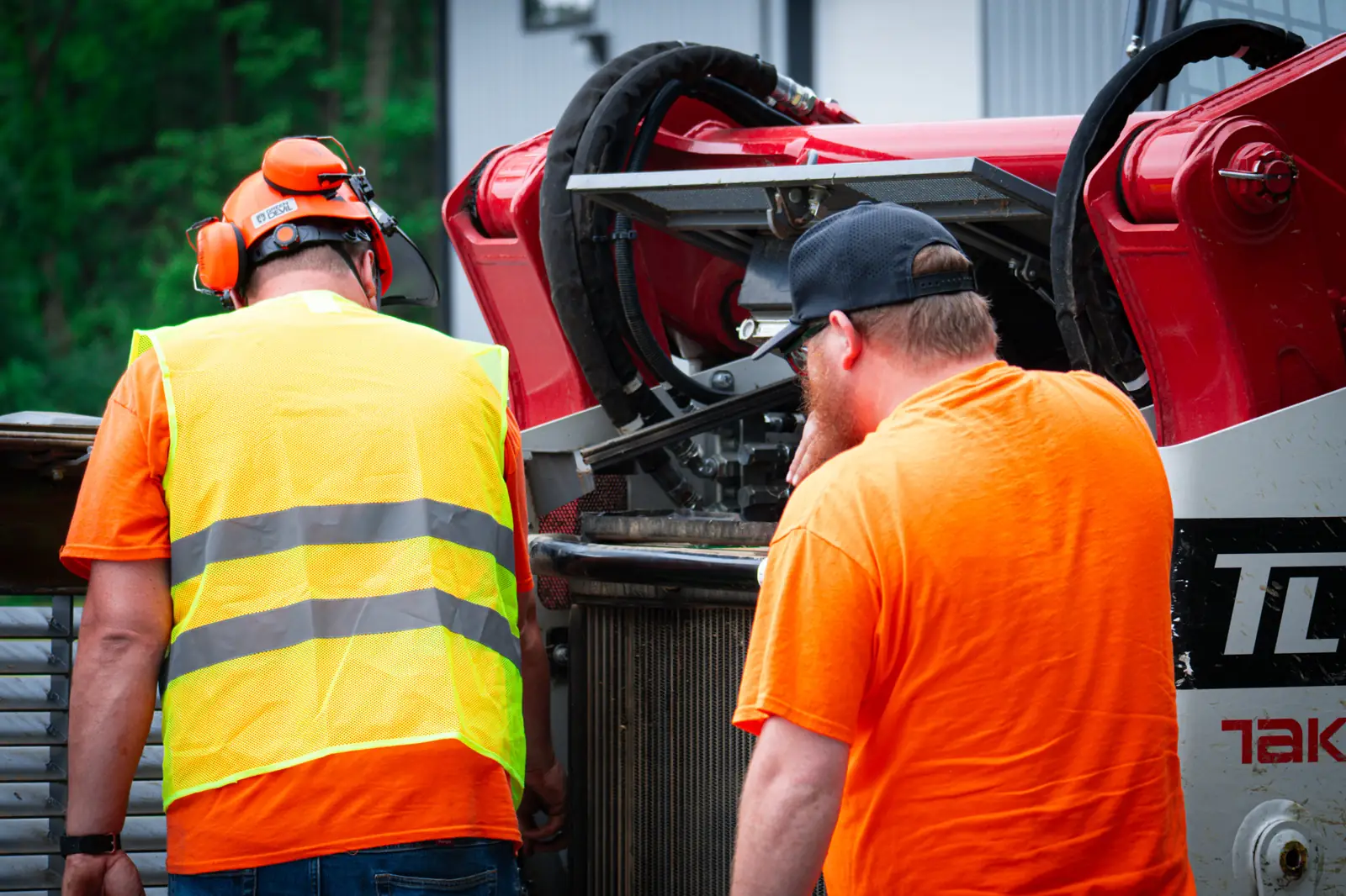 Brushworks operator in hi-vis running pre-start checks on a Takeuchi track loader with a crew member