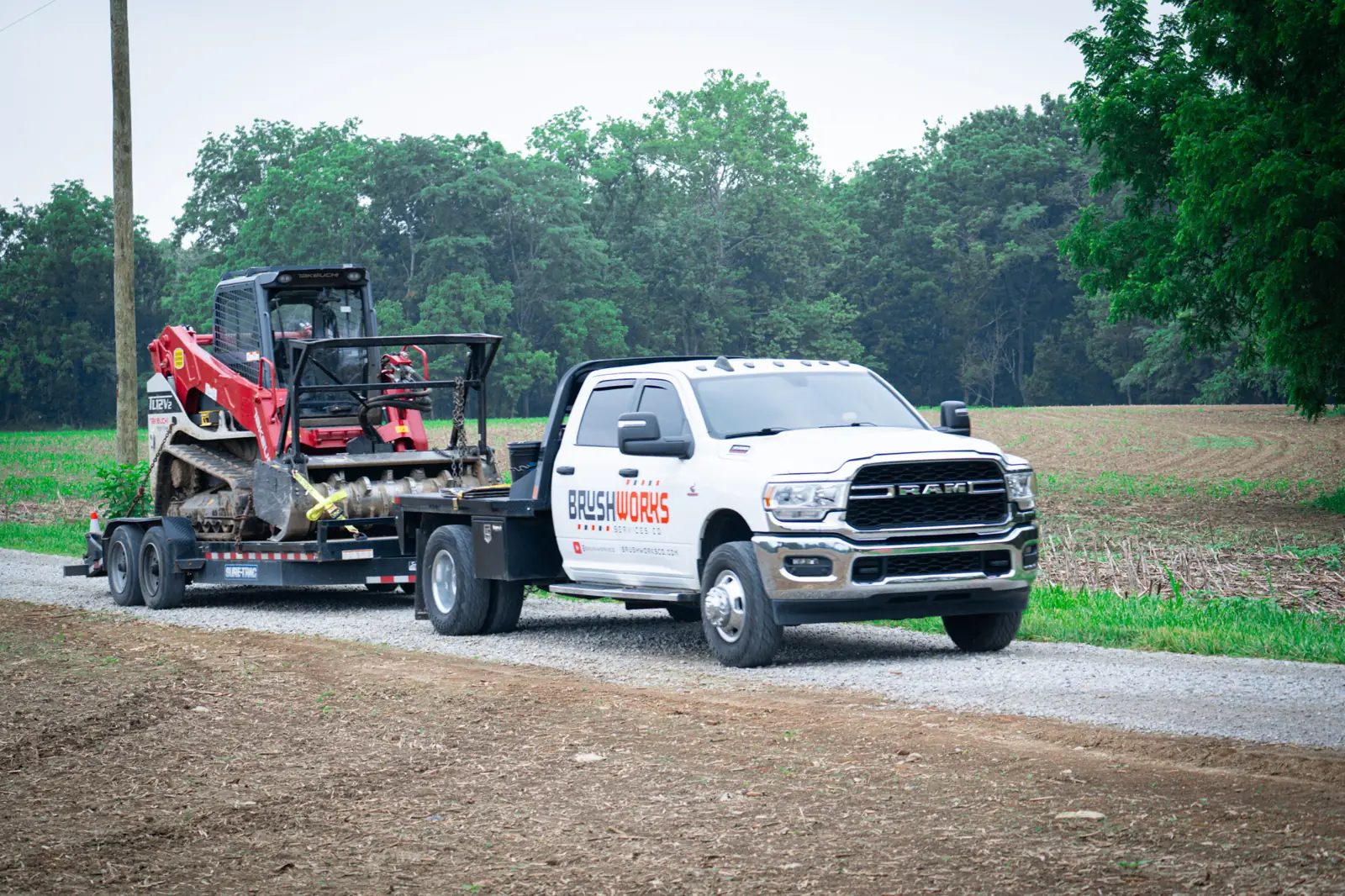 Brushworks RAM truck pulling a Takeuchi track loader on a trailer into a job