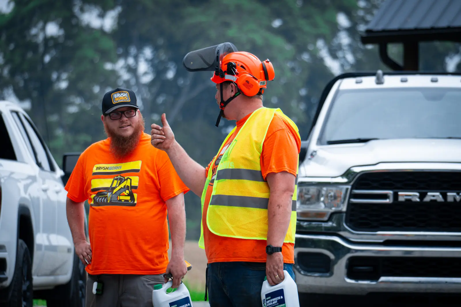 Two Brushworks crew members in orange shirts talking on a job site, one giving a thumbs up