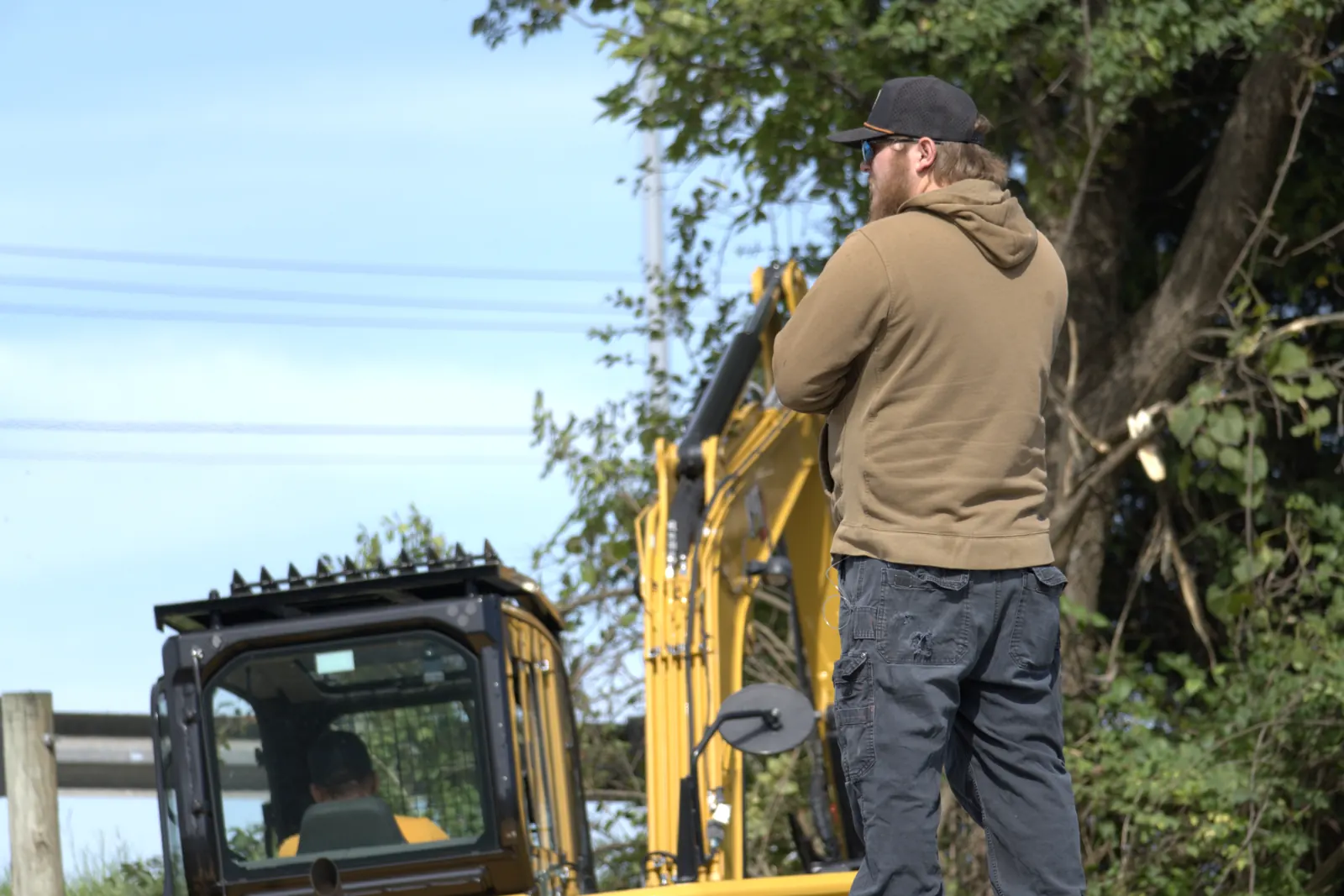 Brushworks crew member watching the work zone while an excavator mulcher clears brush along a corridor