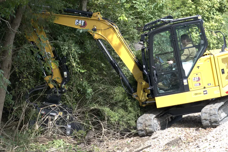 Excavator with a mulching head reaching into a tree line
