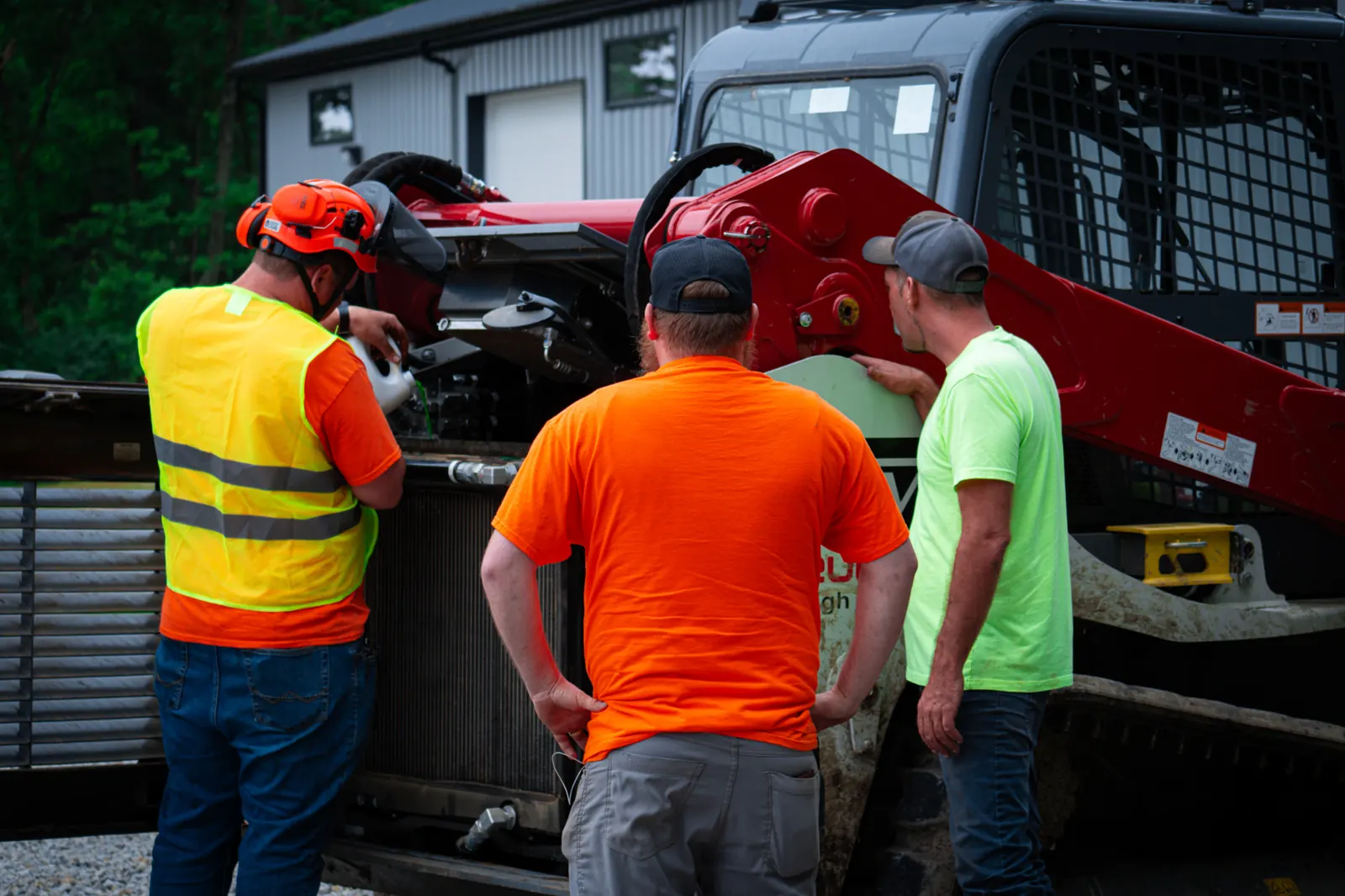Three Brushworks crew members talking through a job beside a Takeuchi track loader