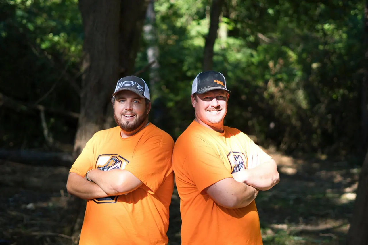 Two Brushworks crew members in orange company shirts in the woods