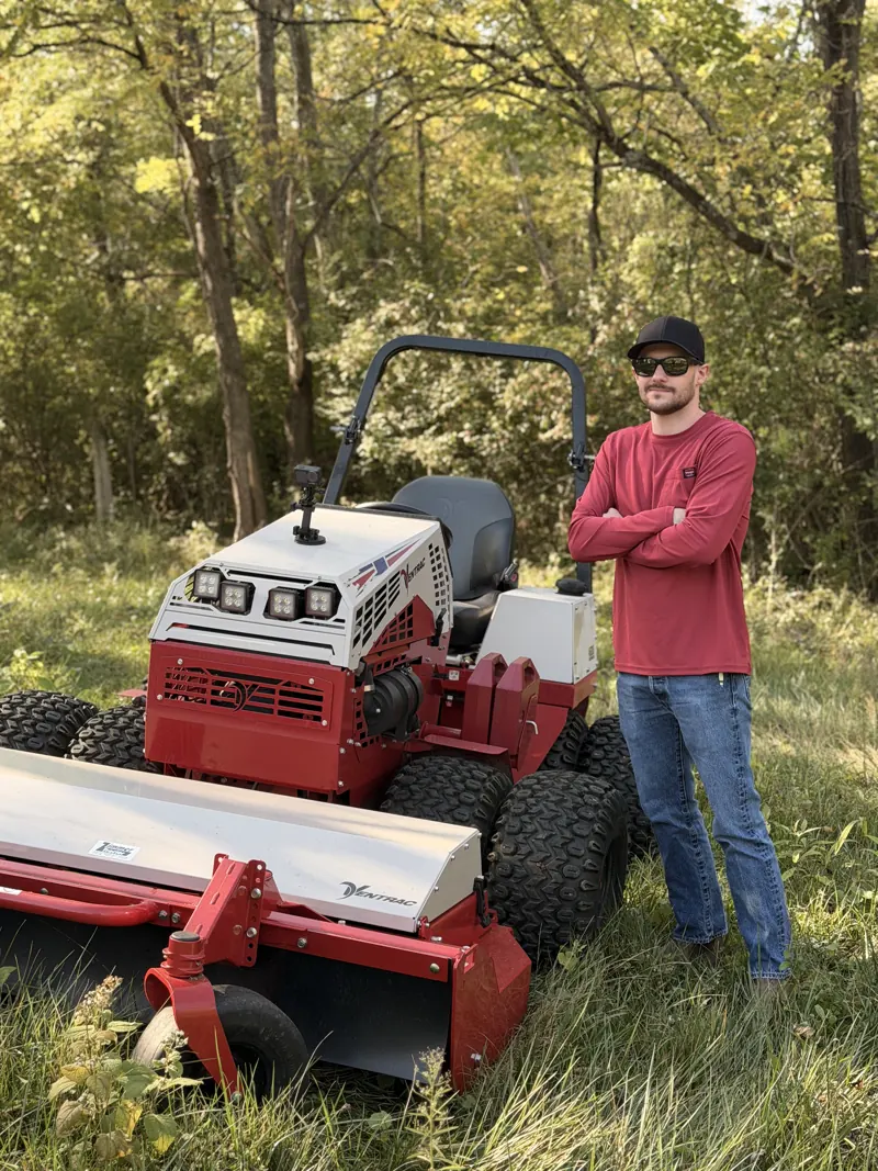 Brushworks operator beside a red brush mower in an open field