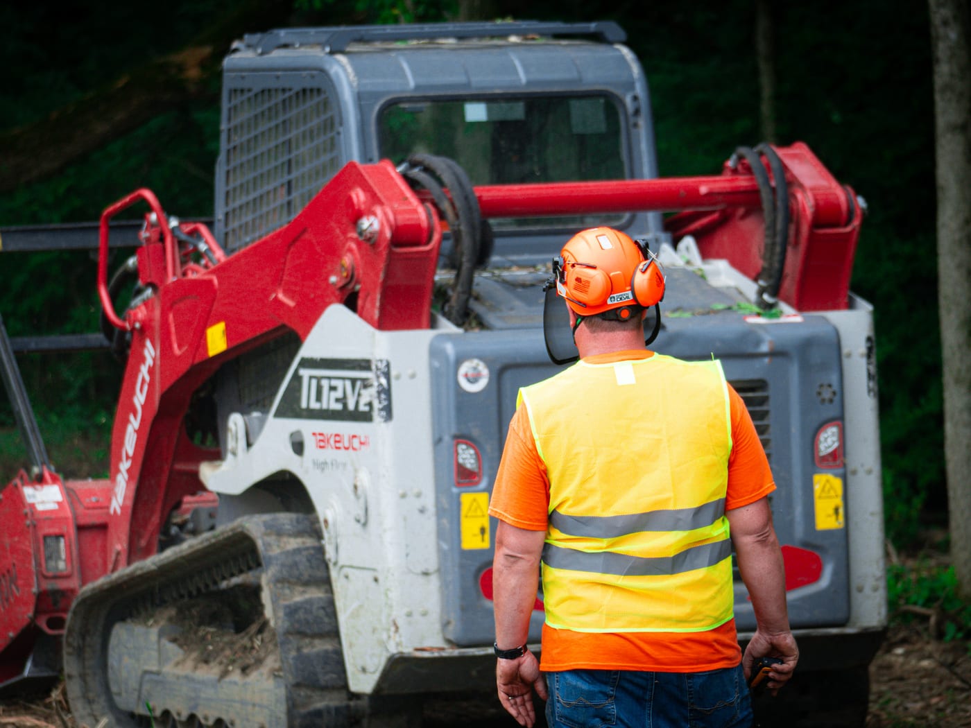 Brushworks team member working behind the Takeuchi loader on a wooded site